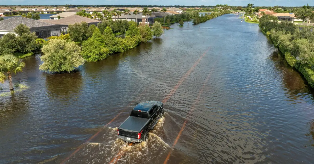 冠水した住宅街の道路を、水しぶきを上げながら走行する黒いピックアップトラックを上空から捉えた様子