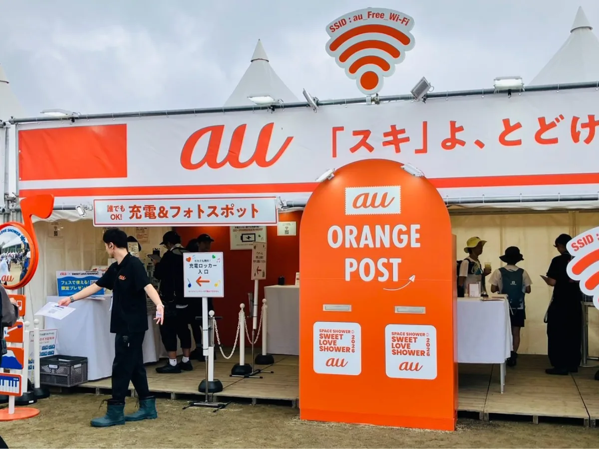 SWEET LOVE SHOWER 2026会場内のauブース。「au『スキ』よ、とどけ」の看板とau ORANGE POSTのオブジェ、SSID：au_Free_Wi-Fiの表示が見える