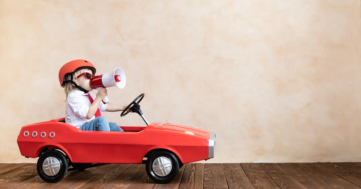 赤いおもちゃの車に乗り、メガホンを口に当てて声を上げる子ども